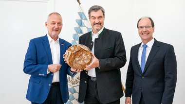 Gespräche mit Ministerpräsident Markus Söder Bild von Landesinnungsmeister Günther Wagner und Geschäftsführer Stephan Kopp und Ministerpräsident Dr. Markus Söder, alle stehen vor einer bayrischen Flagge und Herr Söder hält ein Leib Brot in den Händen